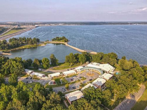 Aerial view of a lakeside facility surrounded by trees and a winding road, with water and a dam in the background.