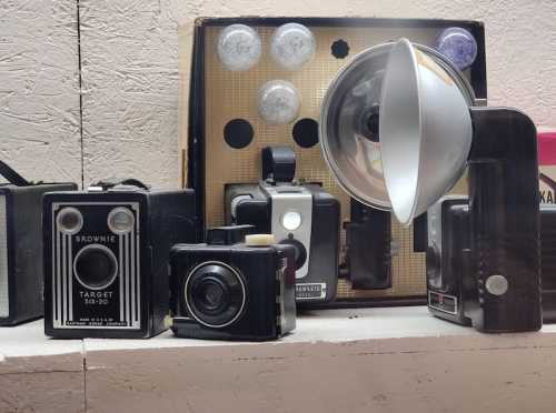 A collection of vintage cameras and a flash, displayed on a shelf against a textured background.