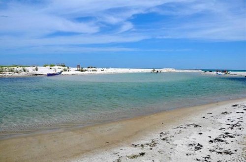 A serene beach scene with calm turquoise water, soft sand, and a clear blue sky.