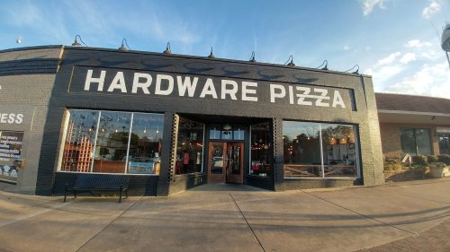 Exterior of Hardware Pizza, featuring large signage, windows, and a welcoming entrance on a sunny day.