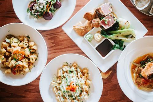 A top-down view of four dishes: pasta, salad, seafood, and assorted appetizers on a wooden table.