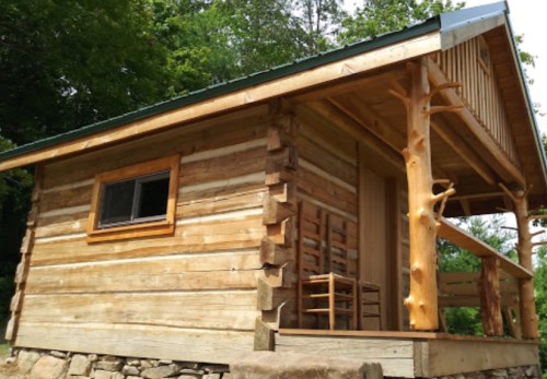 A rustic wooden cabin with a porch, surrounded by trees and featuring a unique log design.