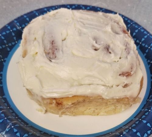 A frosted cinnamon roll on a blue-patterned plate, showcasing its creamy icing and swirled cinnamon filling.