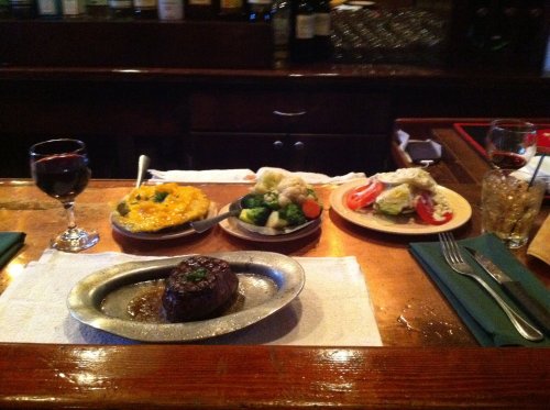 A table setting with a steak, sides of broccoli and cauliflower, a salad, and glasses of red wine.