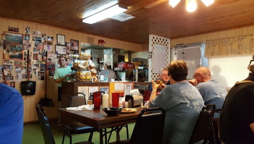 A cozy diner scene with patrons eating at tables, a counter with snacks, and walls decorated with photos.