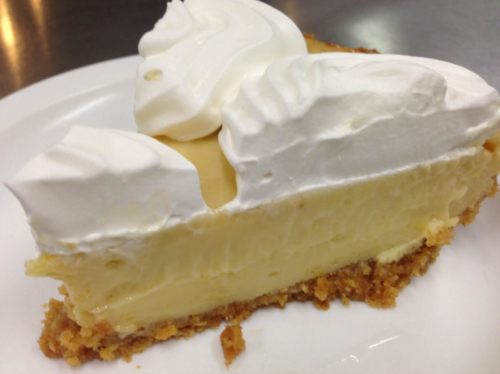 A slice of creamy pie topped with whipped cream on a graham cracker crust, served on a white plate.