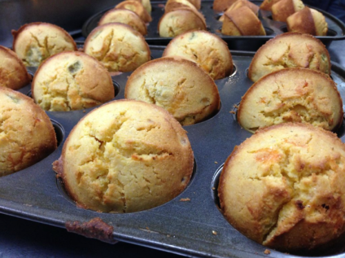 Freshly baked muffins in a metal tray, golden brown with a slightly cracked top.