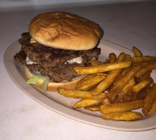 A double cheeseburger with melted cheese and mayonnaise, served with a side of golden French fries on a plate.