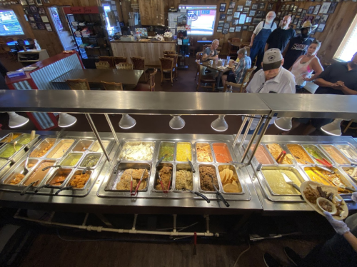 A bustling restaurant buffet with various dishes, diners enjoying meals, and staff serving food in a cozy setting.