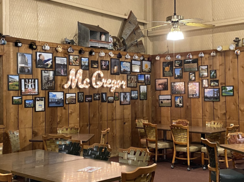 Cozy restaurant interior with wooden walls, a "McGregors" sign, and a gallery of framed photos. Tables and chairs are set up.