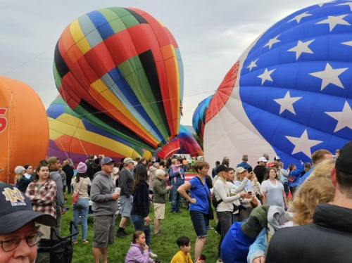 Colorful hot air balloons fill the sky as a crowd gathers on the ground at a festival.