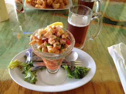 A glass dish of seafood salad with diced vegetables, served with a slice of lemon, alongside a mug of beer and lettuce.