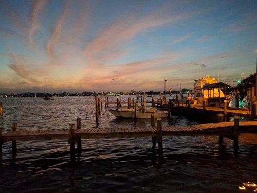 A serene waterfront scene at dusk, featuring boats docked by a wooden pier under a colorful sky.
