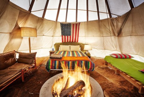 Cozy interior of a tent with a fire pit, colorful bedding, and an American flag hanging on the wall.