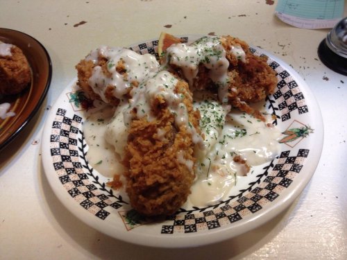 A plate of fried chicken pieces topped with creamy white sauce and sprinkled with herbs.