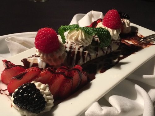 A dessert plate featuring sliced strawberries, blackberries, whipped cream, and chocolate drizzle, garnished with raspberries.