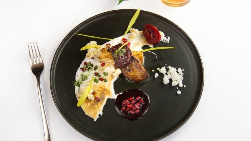 A gourmet dish featuring fish, colorful garnishes, and sauces, elegantly arranged on a black plate.