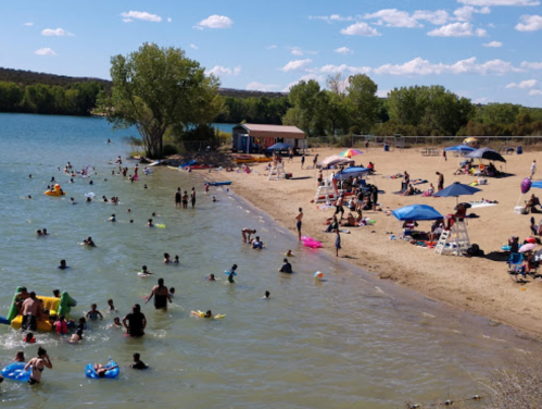A busy beach scene with people swimming, sunbathing, and enjoying the water on a sunny day.