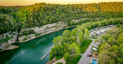 Aerial view of a river surrounded by lush greenery, with a campground and parked RVs along the shore.