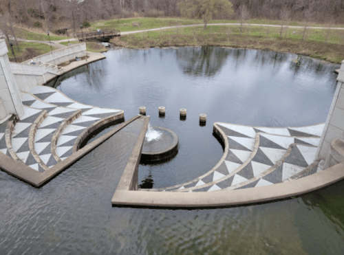 A geometric fountain design in a circular pond, surrounded by greenery and pathways.