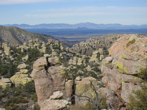 A scenic view of rocky formations and mountains under a clear blue sky, showcasing a rugged desert landscape.