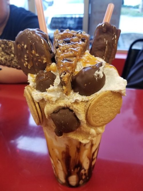A decadent milkshake topped with cookies, chocolate, caramel, and whipped cream, served in a tall glass.