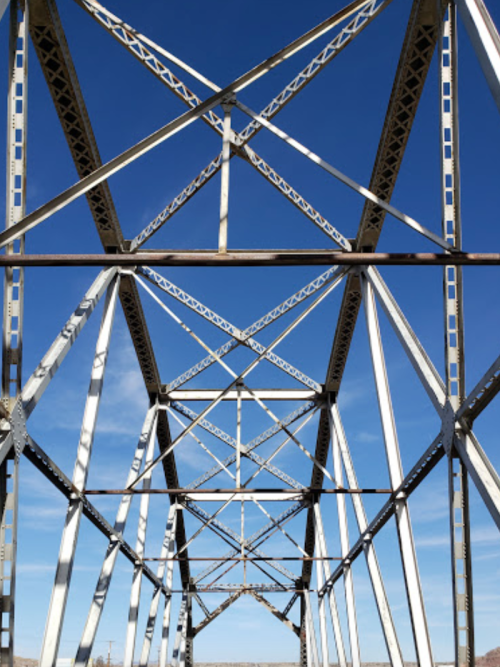 View of a metal bridge's intricate framework against a clear blue sky.