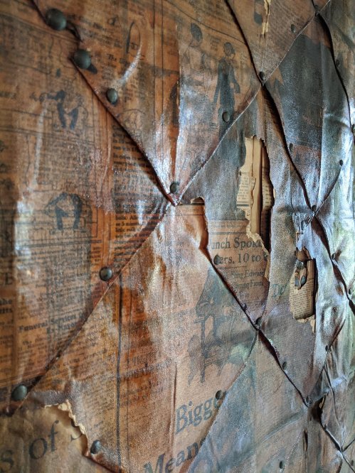 Close-up of aged, textured paper with newspaper clippings, showing wrinkles, tears, and decorative metal fasteners.