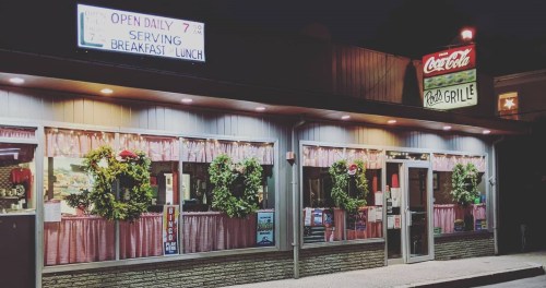 A cozy diner with festive wreaths on the windows, illuminated signs, and a welcoming entrance.