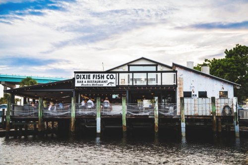 A waterfront restaurant named Dixie Fish Co. with outdoor seating and a cloudy sky in the background.