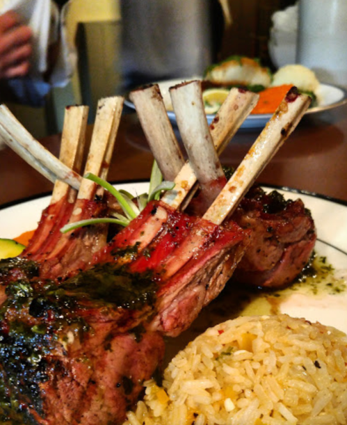 A close-up of grilled lamb chops with herbs, served with rice and garnished with vegetables on a plate.