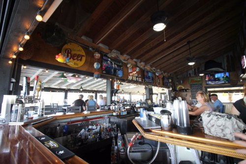A lively bar interior with a wooden ceiling, shelves of drinks, and patrons enjoying the atmosphere.