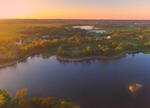 Aerial view of a serene landscape at sunset, featuring a calm river, lush greenery, and distant fields.