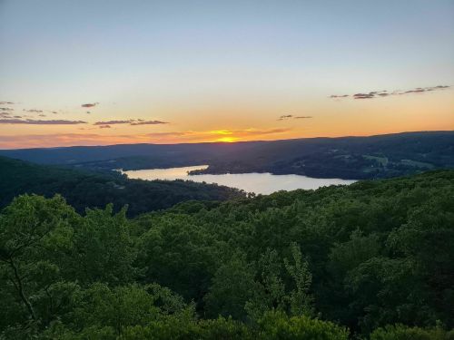 A serene sunset over a lake, surrounded by lush green hills and a clear sky.
