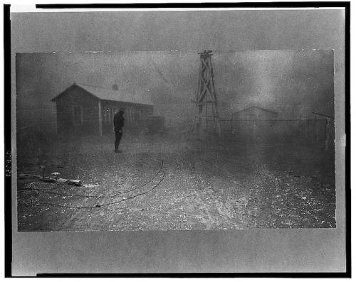 A foggy scene featuring a lone figure near a building and a windmill, with a desolate landscape in the background.