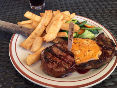 A grilled steak topped with seasoning, served with fries and a side of mixed vegetables on a plate.