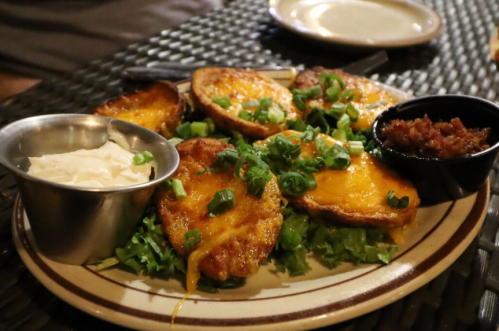 A plate of fried potato slices topped with cheese and green onions, served with sour cream and salsa on the side.