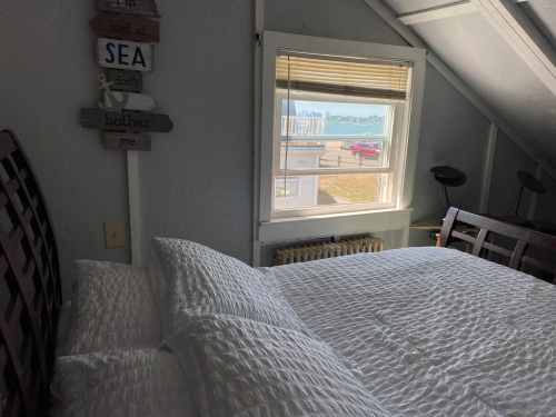 Cozy bedroom with a bed, window showing a view of the sea, and decorative signs on the wall.