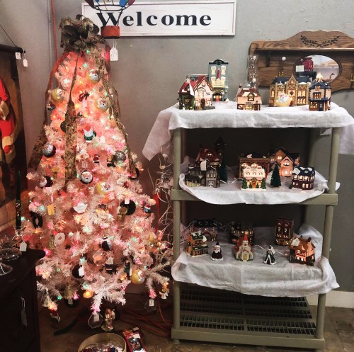 A festive display featuring a pink Christmas tree and a shelf of decorative houses in a cozy shop setting.