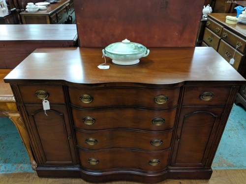 A wooden sideboard with curved edges and multiple drawers, topped with a decorative dish.