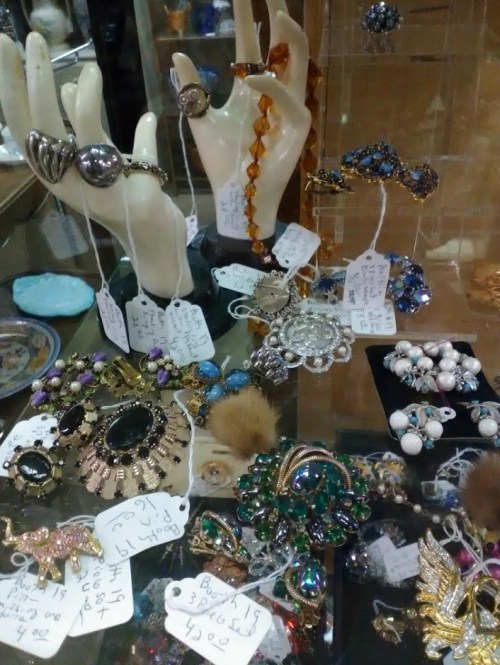 A display of various vintage jewelry pieces, including rings, brooches, and bracelets, with price tags attached.