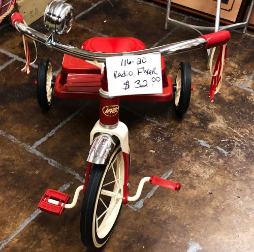 A vintage red Radio Flyer tricycle with a price tag of $32 displayed on the handlebars.