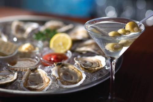 A platter of fresh oysters on ice, accompanied by a martini with olives and lemon.