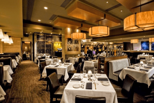 Elegant restaurant interior with white tablecloths, dim lighting, and stylish decor, featuring tables set for dining.