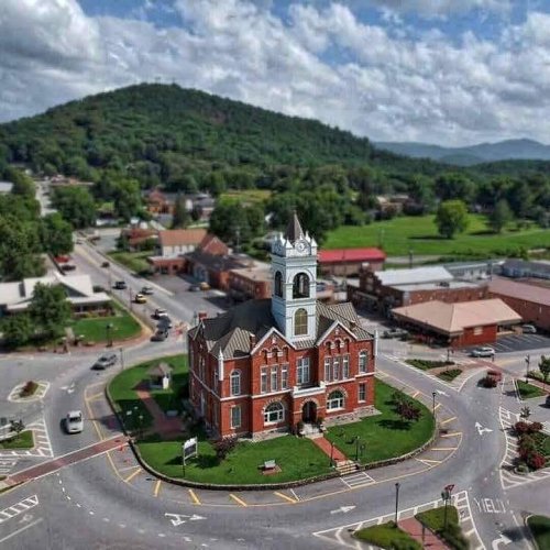 Aerial view of a historic red brick courthouse surrounded by a circular road and green hills in the background.