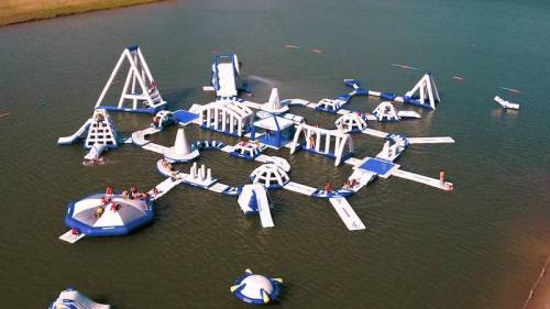 Aerial view of a large inflatable water park with various slides and obstacles on a lake.