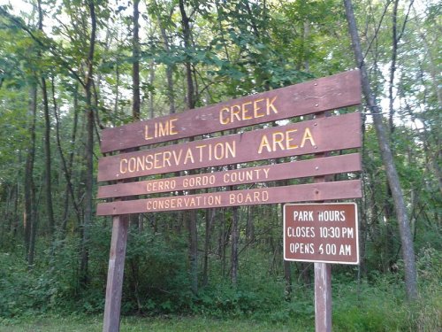 Wooden sign for Lime Creek Conservation Area, listing park hours and managed by Cerro Gordo County Conservation Board.