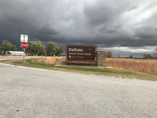 Sign for DeSoto National Wildlife Refuge with dark, cloudy skies and tall grass in the background.