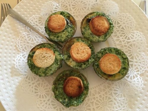 A plate of six green herb and bread round appetizers, garnished and arranged on a decorative doily.