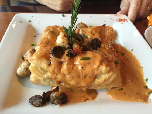 A flaky pastry topped with creamy sauce, shrimp, mushrooms, and a sprig of rosemary, served on a white plate.